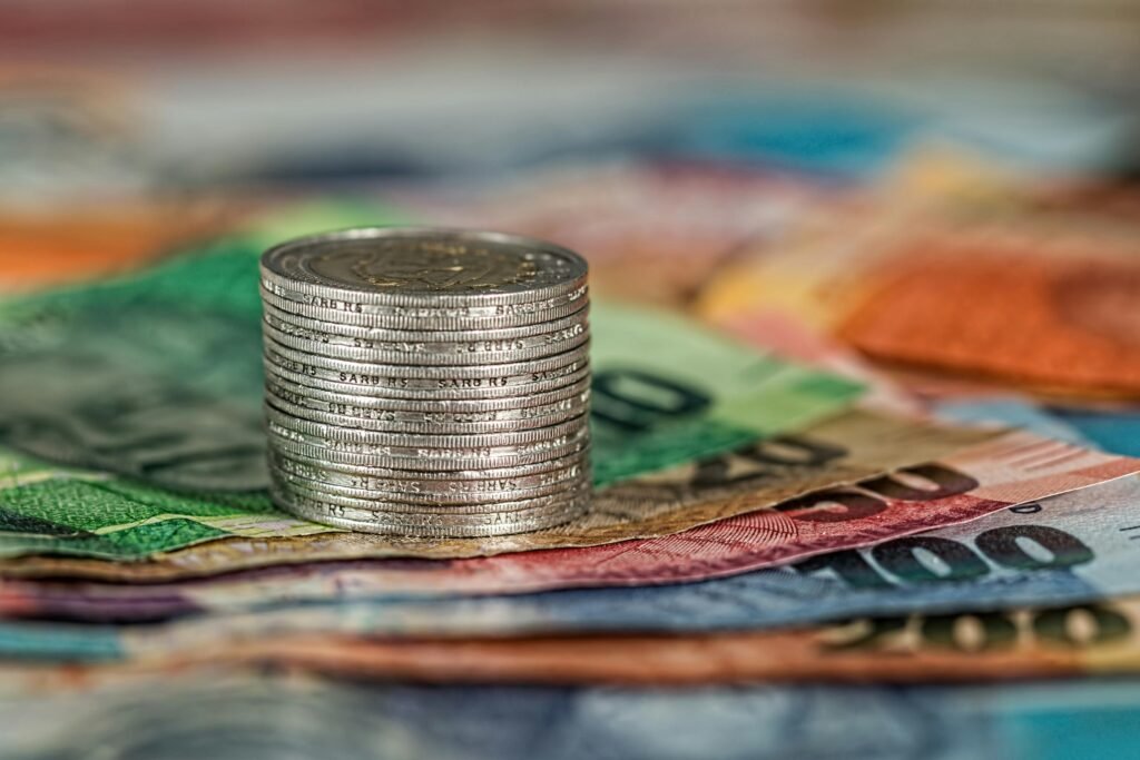 A stack of coins on top of various colored banknotes, symbolizing finance and currency.